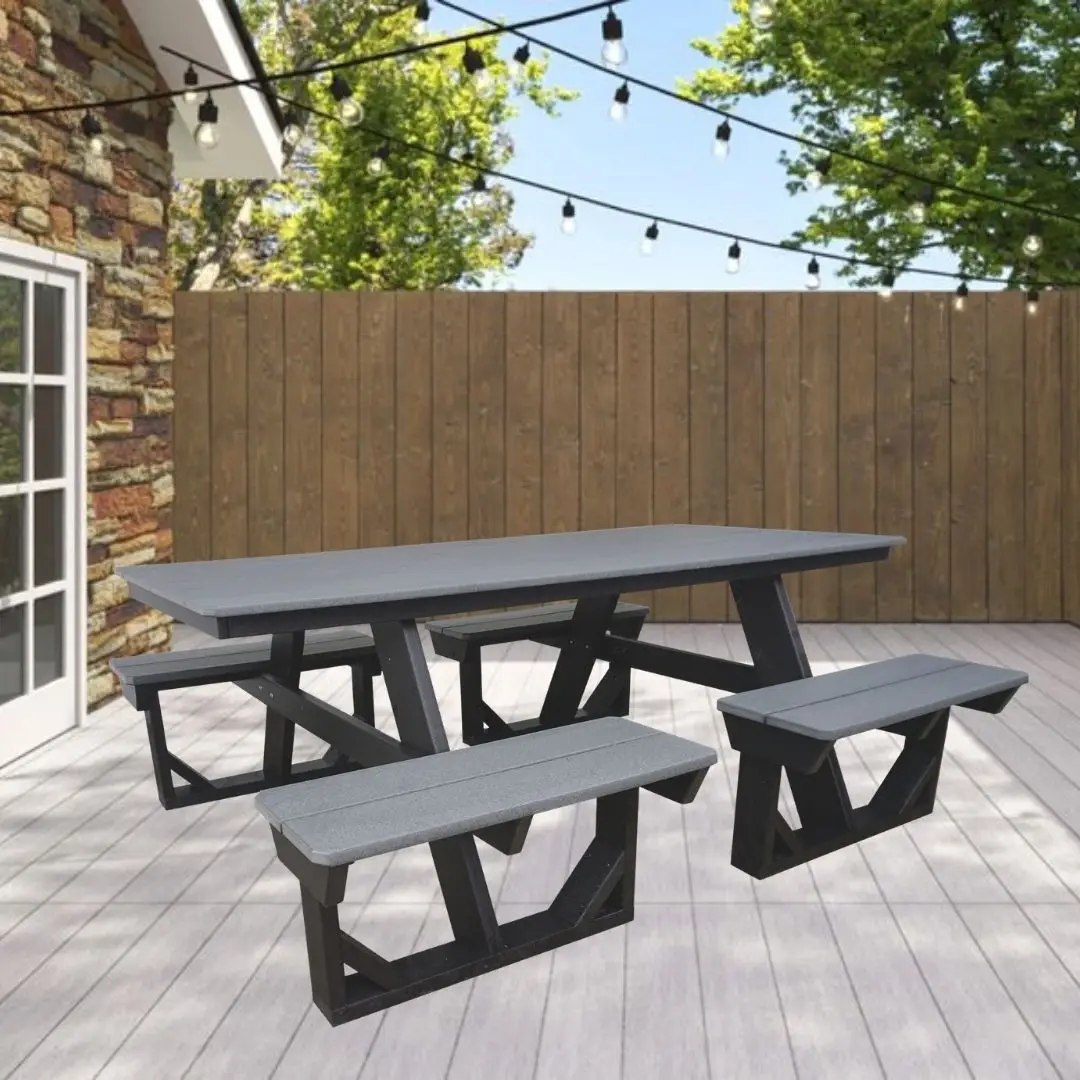 Outdoor backyard scene with a gray-painted wooden picnic table and benches on a light deck, string lights overhead, a wooden privacy fence, and leafy trees in the background.