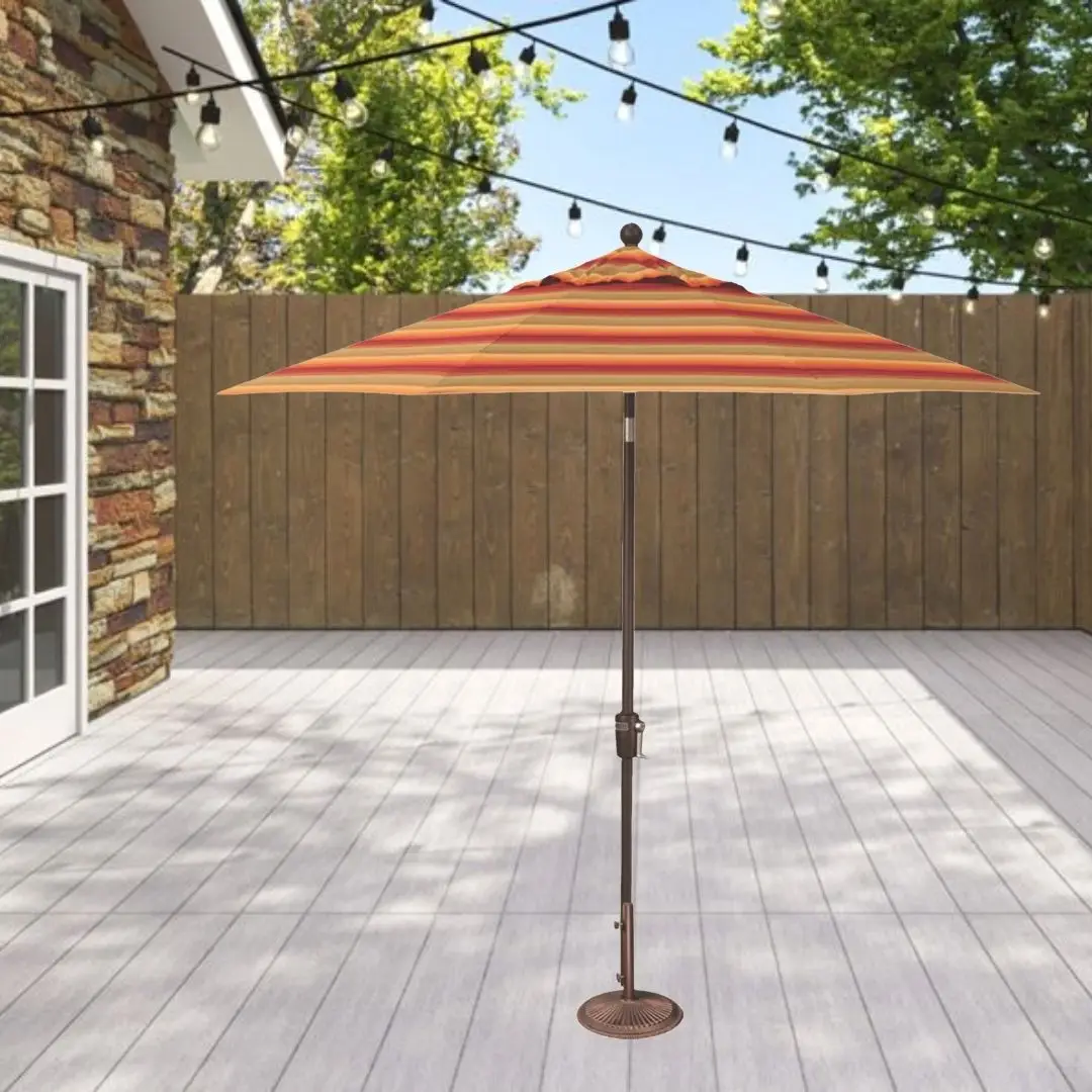 Orange striped patio umbrella on a stand over a light wooden deck with string lights and a wooden privacy fence behind it, in a sunny backyard.