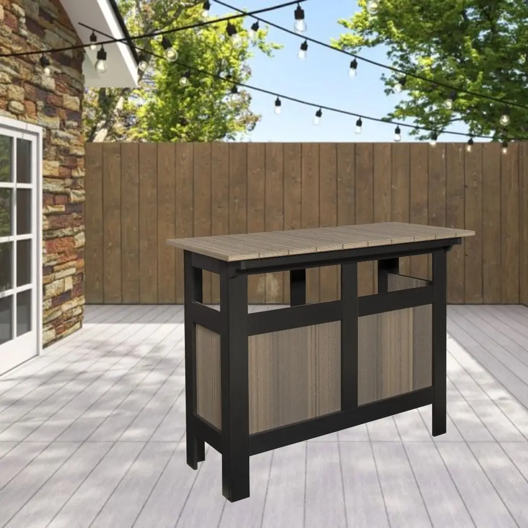 Outdoor backyard bar with a wooden top and black frame on a light deck, string lights overhead, brick wall on the left, and wooden fence in back.
