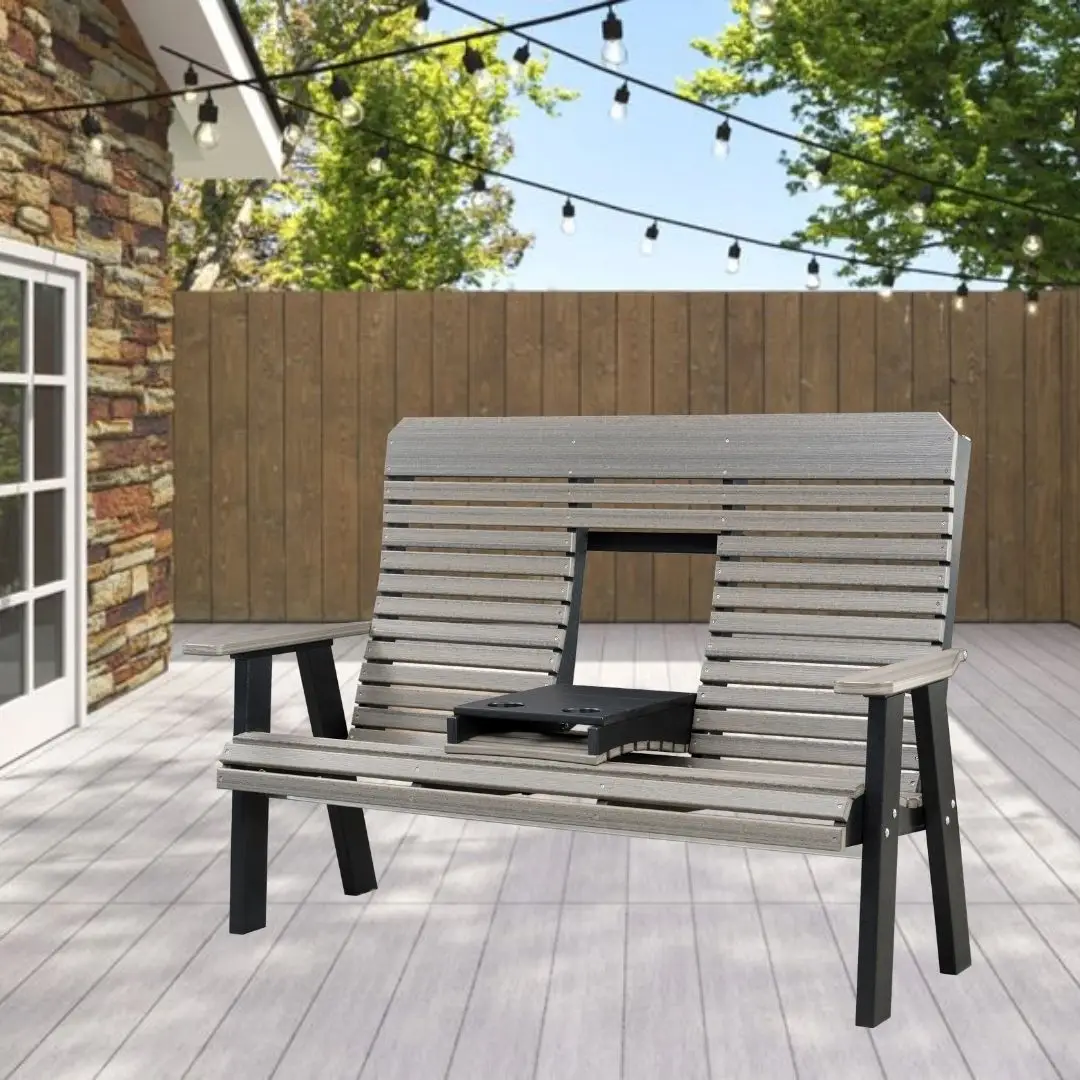Outdoor wooden slatted bench with a built-in grill in the center on a patio, string lights overhead and a wood privacy fence in the background.