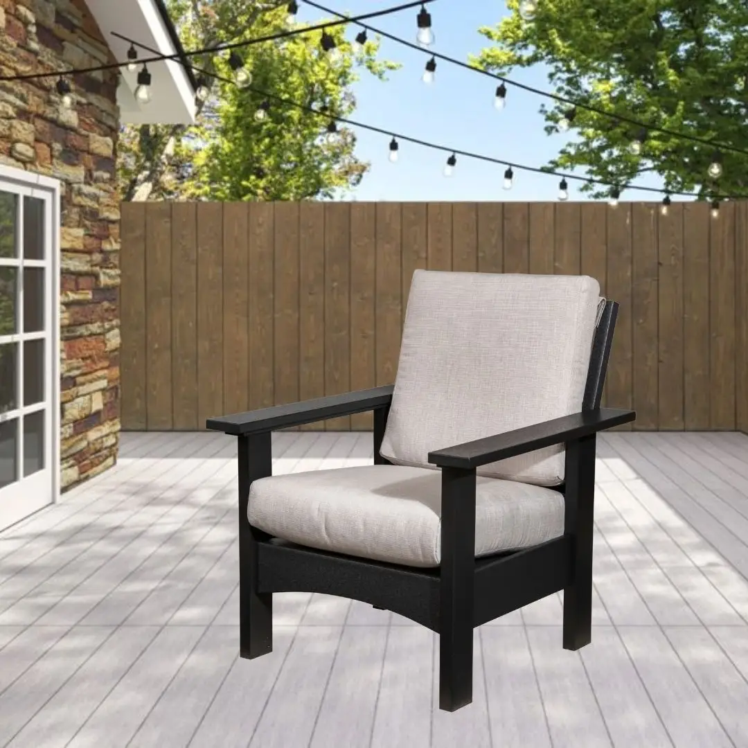 Black wooden outdoor chair with light beige cushions on a wood deck, string lights overhead and a wooden privacy fence in the background.